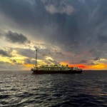 FPSO Almirante Barroso, a 5ª plataforma em produção no Campo de Búzios; com céu acinzentado e encoberto de nuvens e sol se ponto ao fundo (Foto Agência Petrobras)