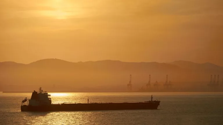 Navio-tanque transporta petróleo com céu em tons de amarelo com pôr do sol, e montanha, ao fundo (Foto Creative Commons)