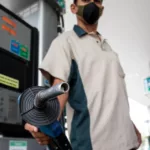 Frentista segura bomba de abastecimento em posto de combustíveis, apontando o bico para a câmera; ao lado, um veículo preto (Foto Agência Petrobras)