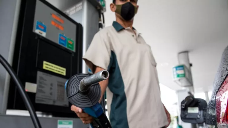 Frentista segura bomba de abastecimento em posto de combustíveis, apontando o bico para a câmera; ao lado, um veículo preto (Foto Agência Petrobras)