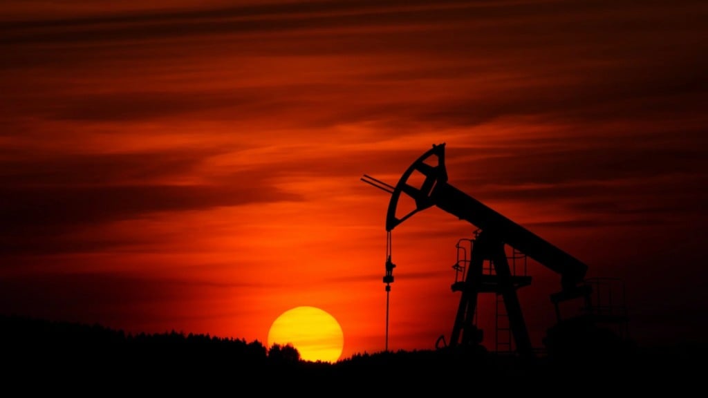 Foto à contraluz de cavalo-de-pau para a exploração de petróleo em terra, com sol se pondo ao fundo e céu alaranjado (Foto Zbynek Burival/Unsplash)