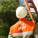 T&eacute;cnico da Light em servi&ccedil;o de reparo &agrave; rede, com equipamentos de seguran&ccedil;a, no alto de uma escada encostada em um poste de eletricidade (Foto Paula Kossatz/Divulga&ccedil;&atilde;o)