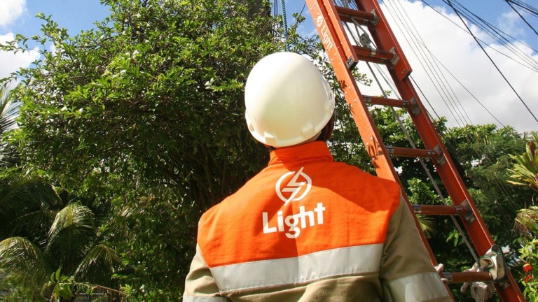 Técnico da Light em serviço de reparo à rede, com equipamentos de segurança, no alto de uma escada encostada em um poste de eletricidade (Foto Paula Kossatz/Divulgação)