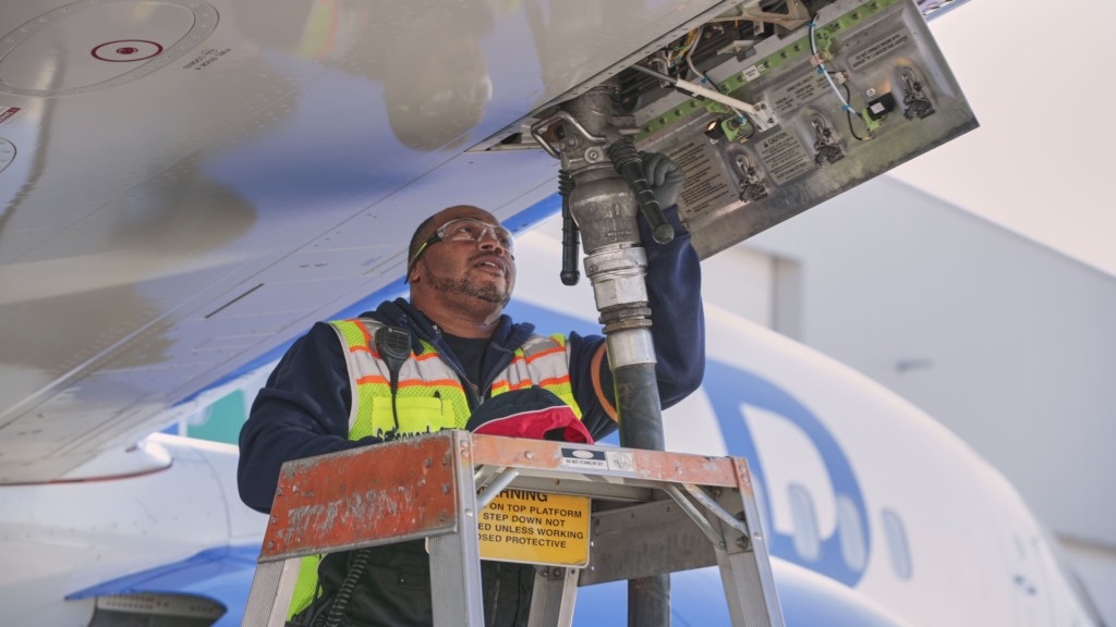 Técnico de manutenção de aviação, com colete de segurança amarelo fosforescente, faz o abastecimento com mangueira conectada verticalmente na parte de baixo da aeronave (Foto Thomas Vangel/Photography) Técnico de manutenção de aviação, com colete de segurança amarelo fosforescente, faz o abastecimento com mangueira conectada verticalmente na parte de baixo da aeronave (Foto Thomas Vangel/Photography)