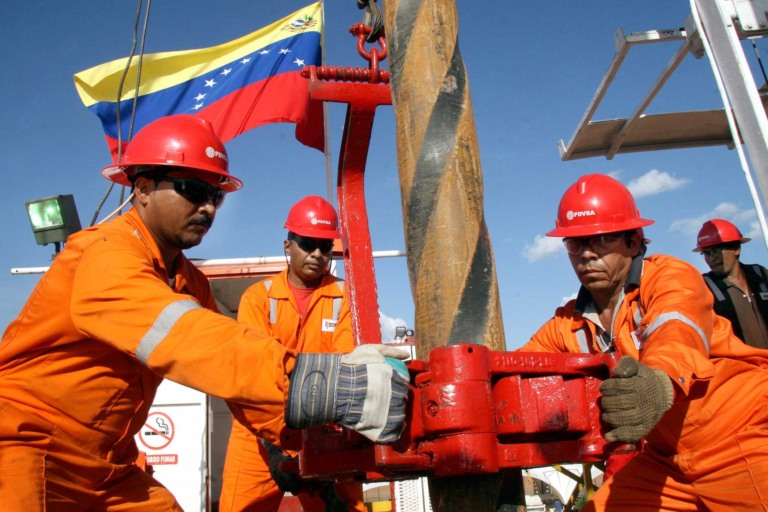 Funcionários da PDVSA, petroleira estatal da Venezuela, operam equipamento de perfuração; uniformizados, em laranja, com equipamentos e sinalizações de segurança e capacete vermelho (Foto Divulgação)