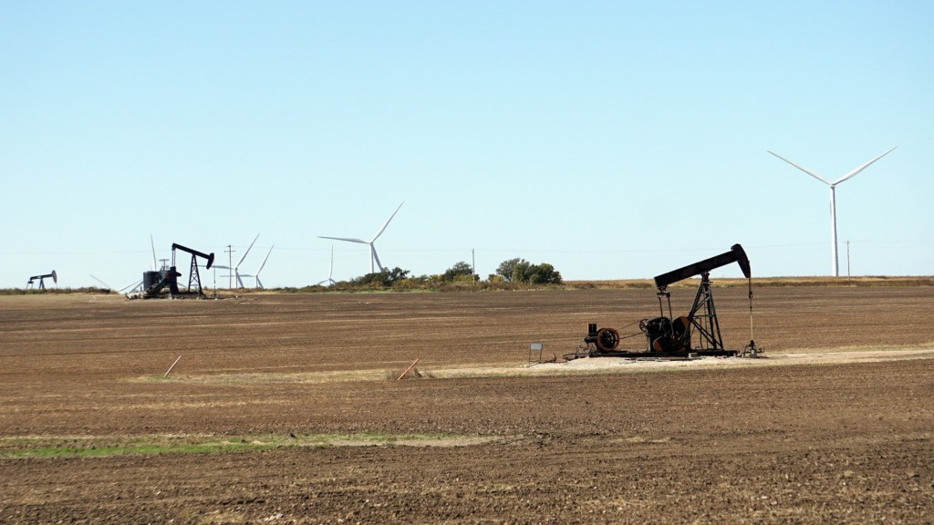 Cavalos-de-pau (bomba 'pumpjack') para a produção onshore de petróleo, em Oklahoma (EUA), com turbinas eólicas ao fundo (Foto Mike/RJA1988/Pixabay) Cavalos-de-pau (bomba 'pumpjack') para a produção onshore de petróleo, em Oklahoma (EUA), com turbinas eólicas ao fundo (Foto Mike/RJA1988/Pixabay)